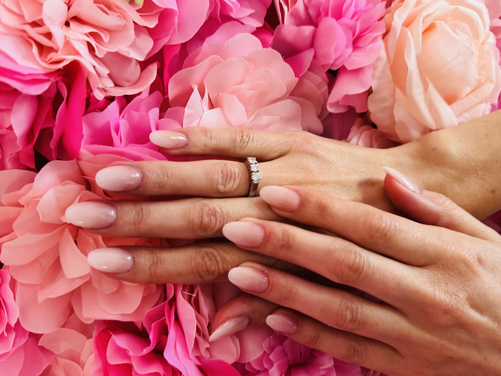 Verzorgde nude nagels met een ring, voor de roze bloemenwand in de salon