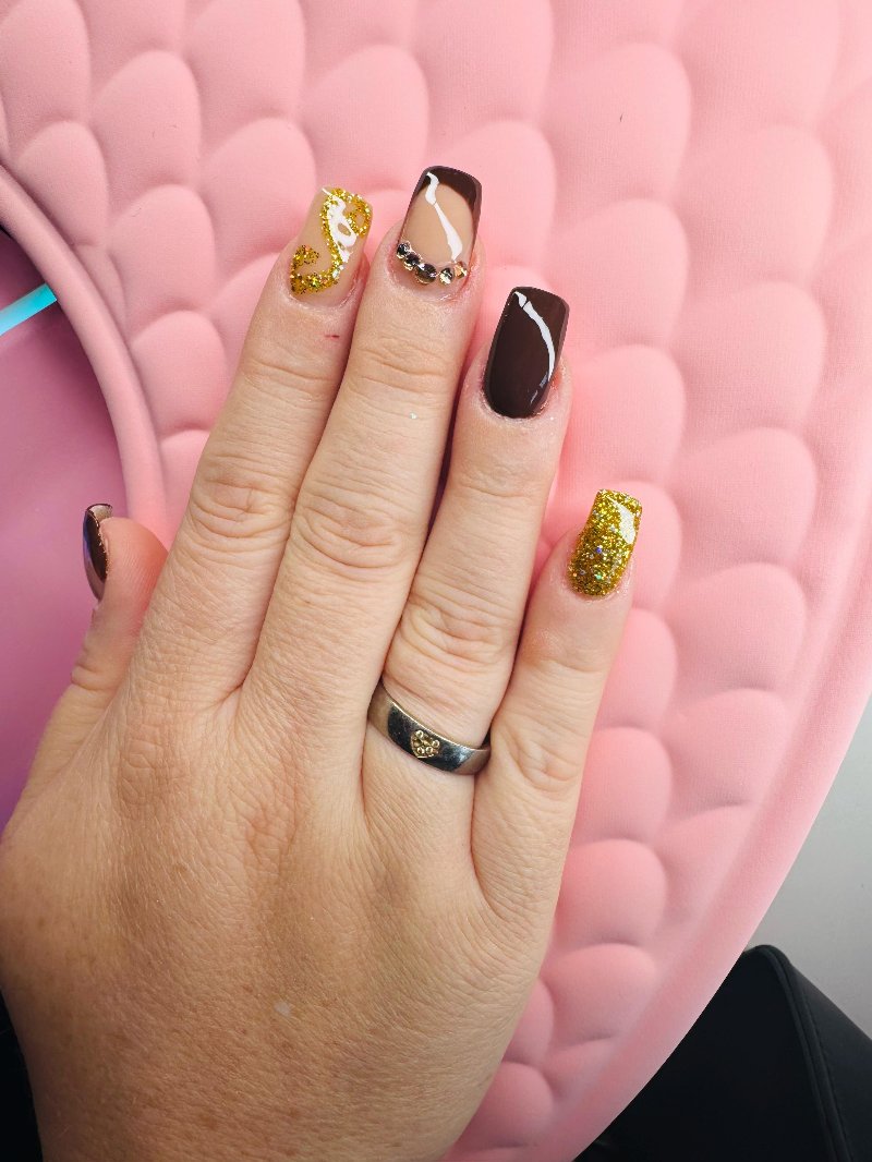 Nagels in goud en bruin met nail art op een roze handkussen